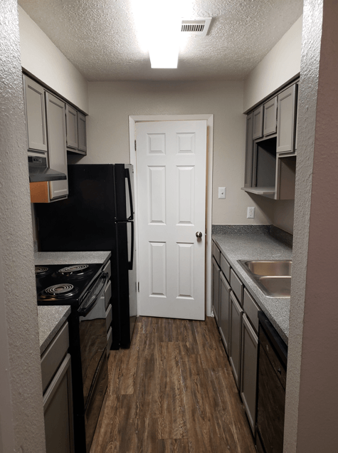 A kitchen with a black refrigerator and wooden floors.